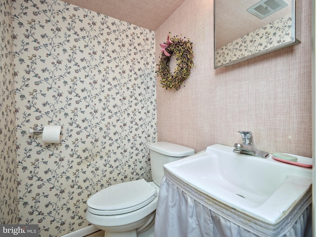 bathroom with toilet, wallpapered walls, visible vents, and a sink