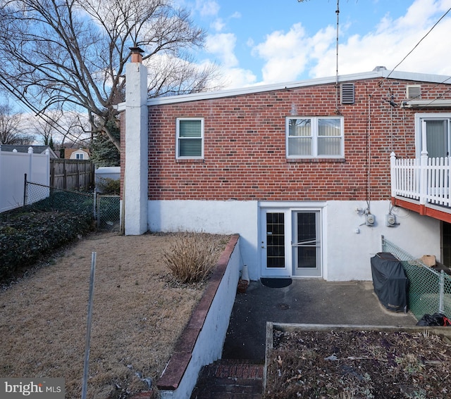 back of house featuring a chimney, fence, and brick siding