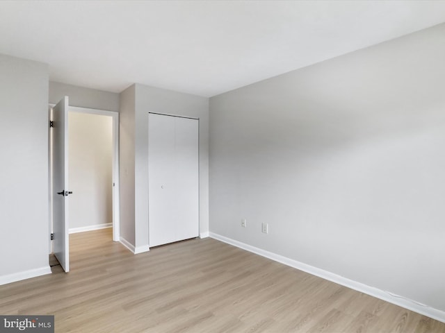 unfurnished bedroom featuring a closet, light wood-style flooring, and baseboards