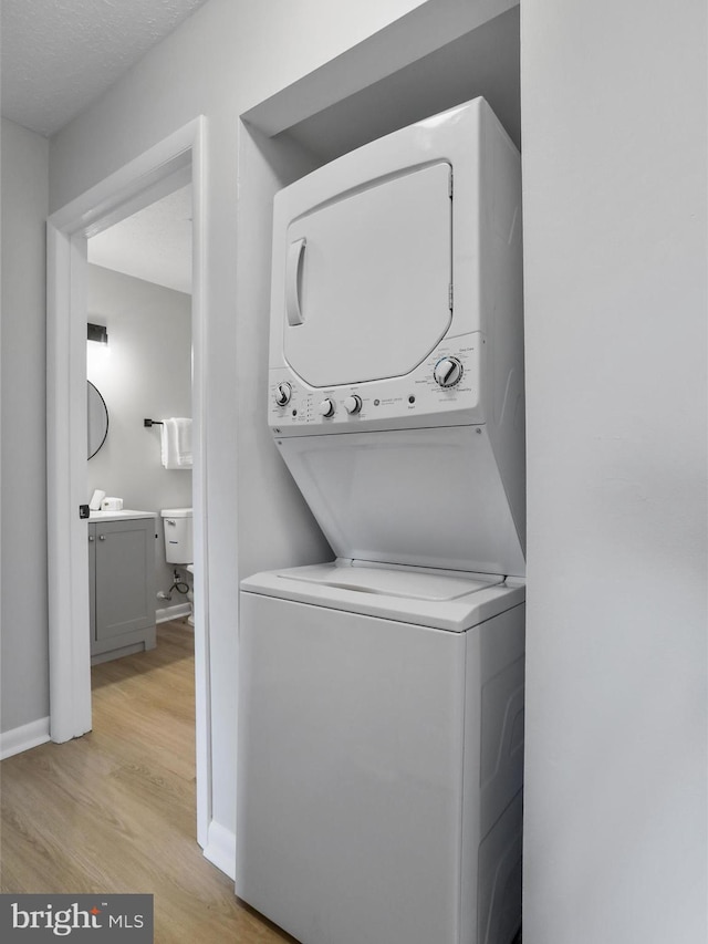 washroom with stacked washer and clothes dryer, baseboards, light wood finished floors, and laundry area