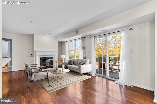 living area featuring a glass covered fireplace, dark wood finished floors, visible vents, and baseboards