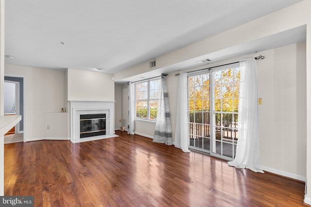 unfurnished living room featuring a fireplace with flush hearth, dark wood-style flooring, visible vents, and baseboards