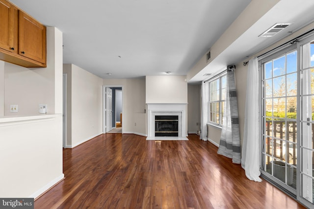 unfurnished living room featuring baseboards, a fireplace with flush hearth, visible vents, and dark wood-type flooring