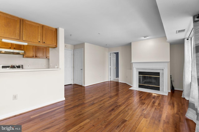 unfurnished living room featuring visible vents, baseboards, a fireplace with flush hearth, dark wood-style flooring, and a sink