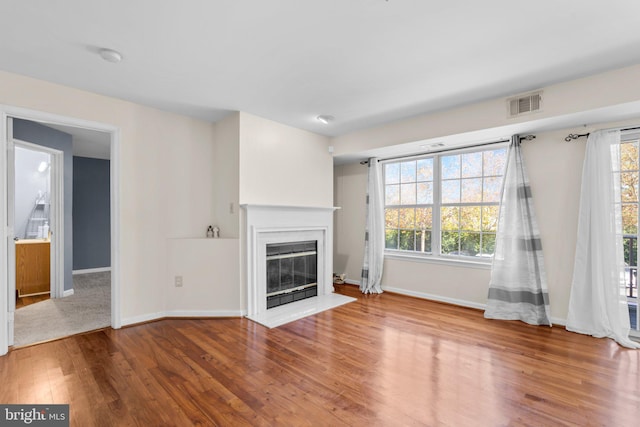 unfurnished living room with a fireplace with flush hearth, a healthy amount of sunlight, visible vents, and wood finished floors