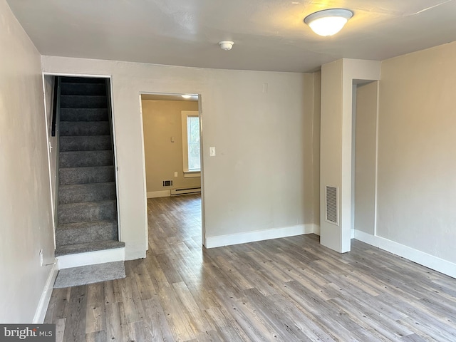 spare room with visible vents, baseboards, a baseboard radiator, stairway, and wood finished floors