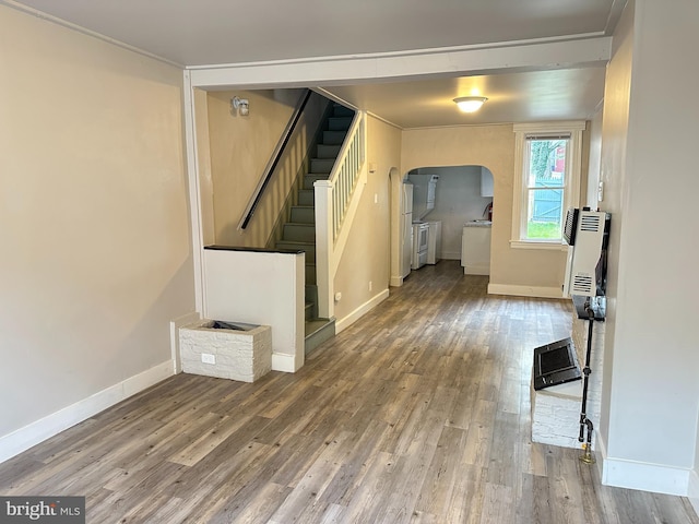 unfurnished living room featuring baseboards, arched walkways, stairway, wood finished floors, and heating unit