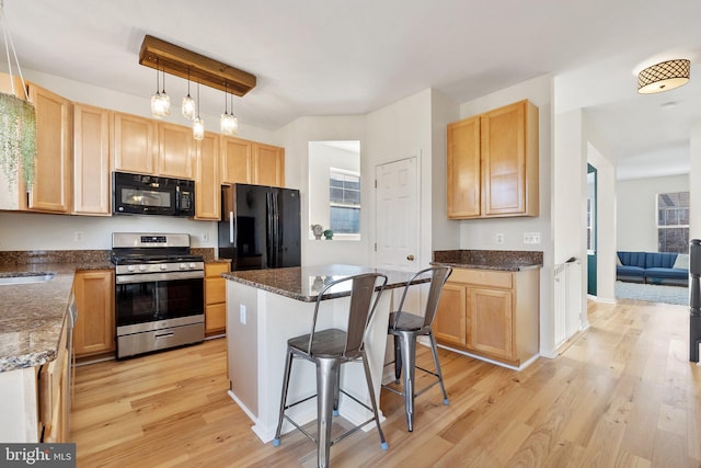 kitchen featuring decorative light fixtures, a sink, black appliances, light wood-type flooring, and a kitchen breakfast bar