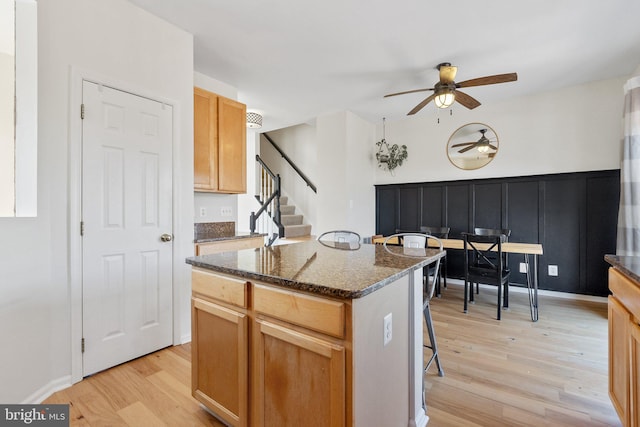 kitchen featuring dark stone counters, a ceiling fan, a kitchen breakfast bar, a center island, and light wood-style floors