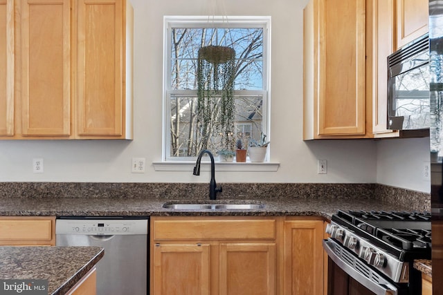 kitchen featuring dark stone counters, stainless steel appliances, a sink, and light brown cabinetry