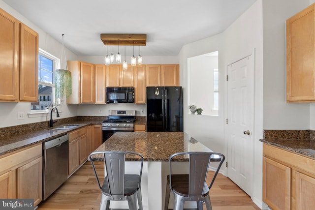 kitchen featuring black appliances, dark stone counters, a breakfast bar, and a sink