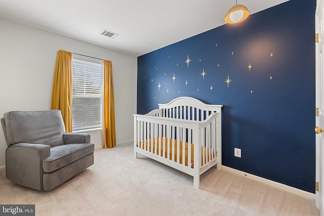 carpeted bedroom with an accent wall, visible vents, a crib, and baseboards