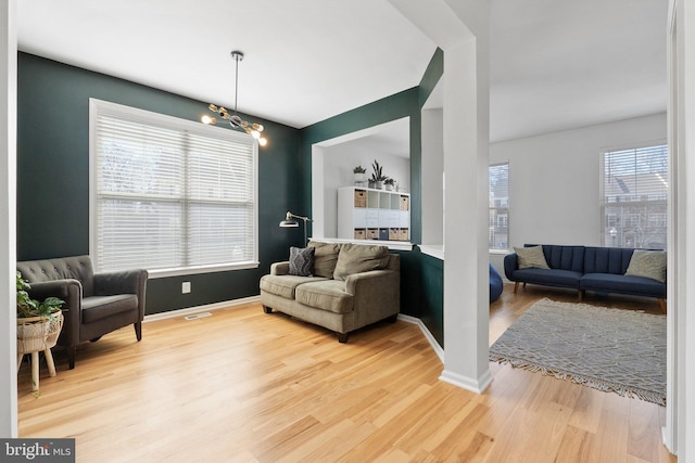 living room featuring an inviting chandelier, visible vents, baseboards, and wood finished floors