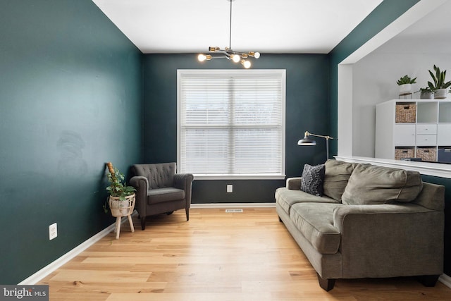 living area featuring baseboards, a notable chandelier, and light wood finished floors