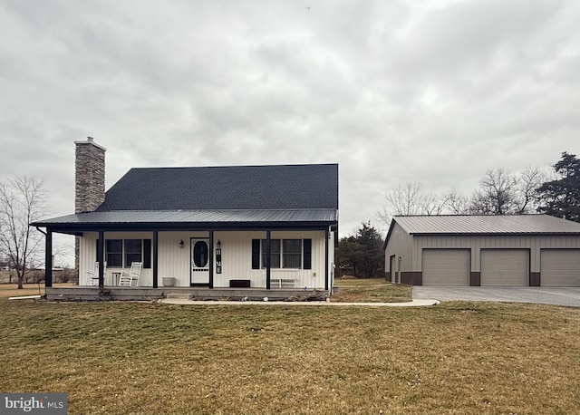 view of front of house with a detached garage, a chimney, a porch, a front yard, and metal roof