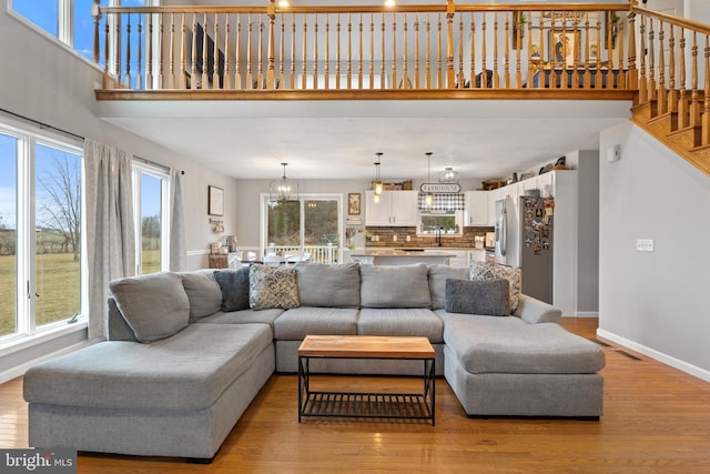 living area featuring visible vents, baseboards, an inviting chandelier, stairs, and light wood-type flooring