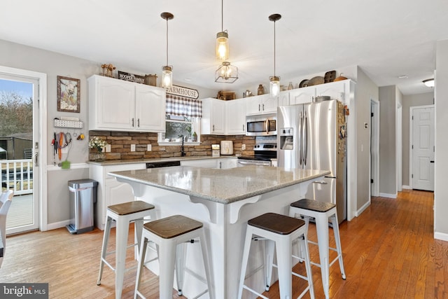 kitchen with light wood finished floors, appliances with stainless steel finishes, white cabinets, and backsplash