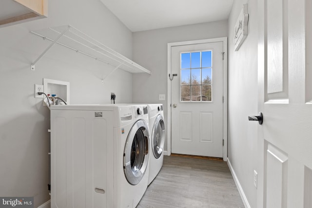 washroom featuring laundry area, washing machine and dryer, baseboards, and light wood-style floors