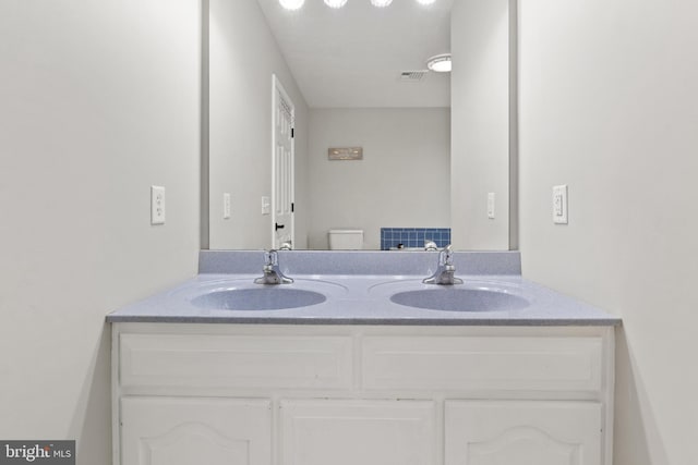 bathroom featuring double vanity, visible vents, toilet, and a sink