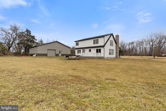 rear view of property featuring a garage, a chimney, a lawn, and an outbuilding