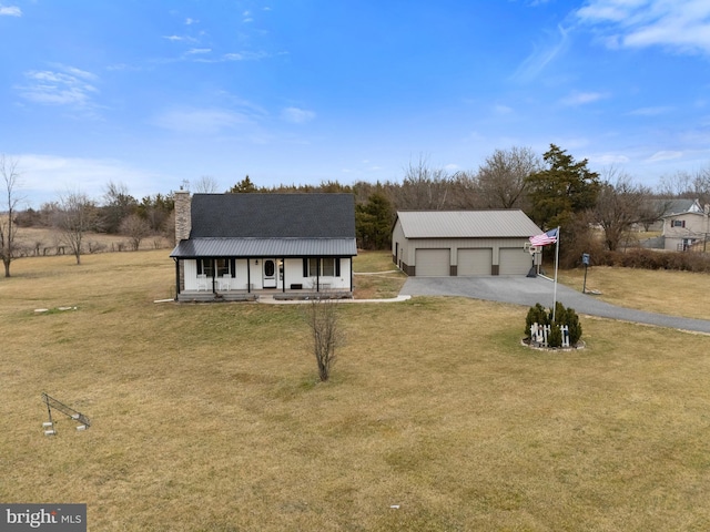 view of front of property featuring a detached garage, a chimney, covered porch, metal roof, and a front lawn