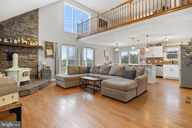 living area featuring a wood stove, baseboards, a towering ceiling, and light wood finished floors