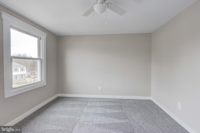 carpeted spare room with a ceiling fan and baseboards