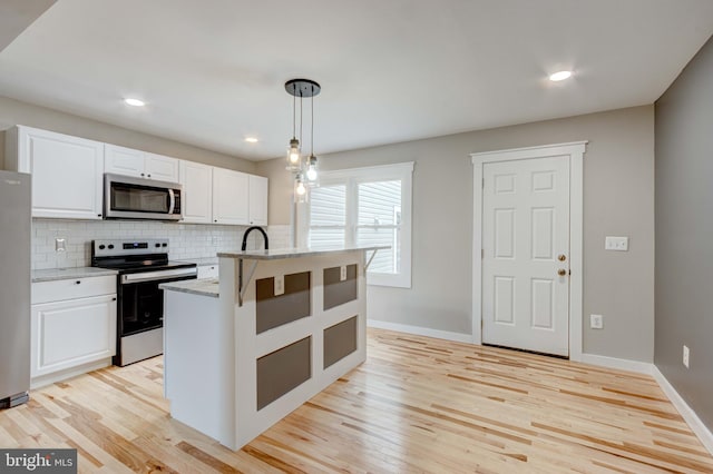 kitchen featuring light stone counters, light wood finished floors, stainless steel appliances, decorative backsplash, and white cabinets