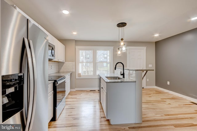 kitchen with light stone countertops, decorative backsplash, appliances with stainless steel finishes, light wood-style floors, and a sink