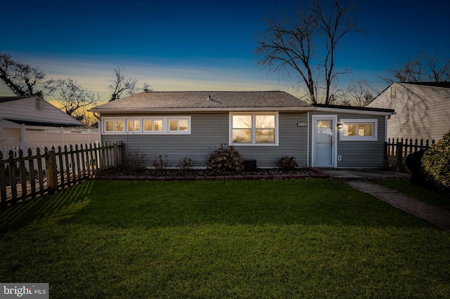 back of property at dusk featuring fence and a lawn