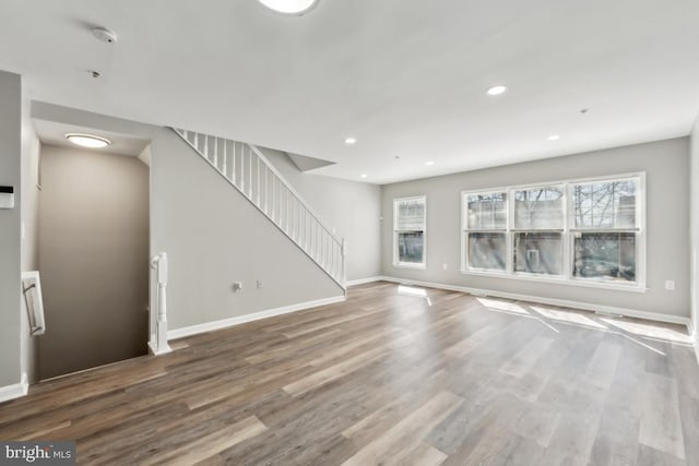 unfurnished living room featuring stairs, recessed lighting, baseboards, and wood finished floors