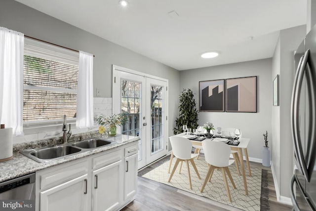 kitchen with light wood finished floors, appliances with stainless steel finishes, french doors, white cabinetry, and a sink