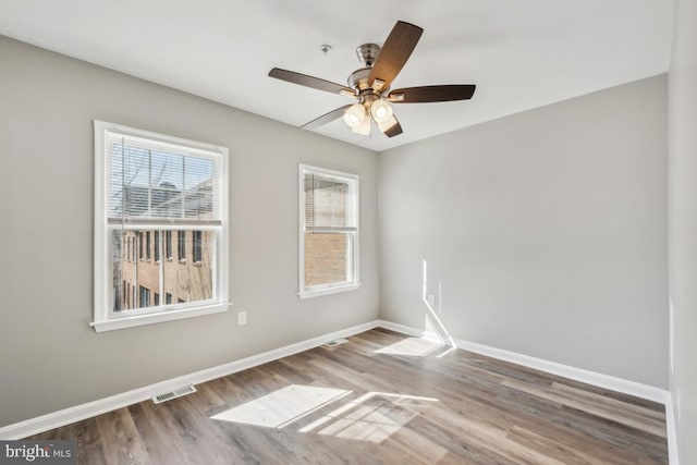 empty room with a ceiling fan, baseboards, visible vents, and wood finished floors