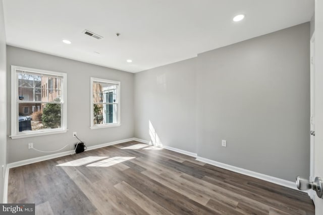 empty room with dark wood-style floors, recessed lighting, visible vents, and baseboards