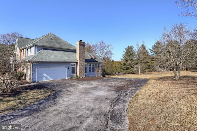 view of side of home featuring aphalt driveway, roof with shingles, a chimney, and a garage