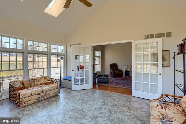 living area with high vaulted ceiling, a skylight, visible vents, and a ceiling fan