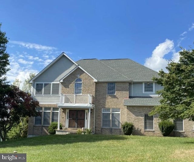 view of front of home featuring a front yard, brick siding, a balcony, and roof with shingles