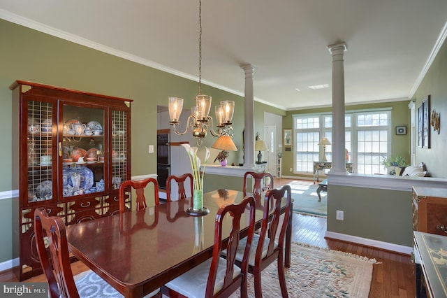 dining area with a notable chandelier, wood finished floors, baseboards, ornamental molding, and ornate columns