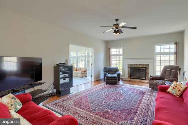 living area featuring a brick fireplace, ceiling fan, a wealth of natural light, and wood finished floors