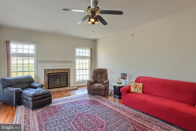 living area with a ceiling fan, a fireplace, and wood finished floors