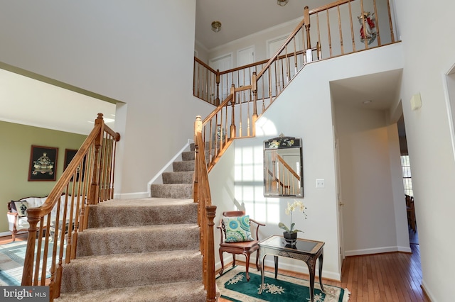 stairway featuring ornamental molding, a towering ceiling, baseboards, and hardwood / wood-style flooring