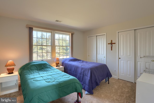 carpeted bedroom with multiple closets, visible vents, and baseboards