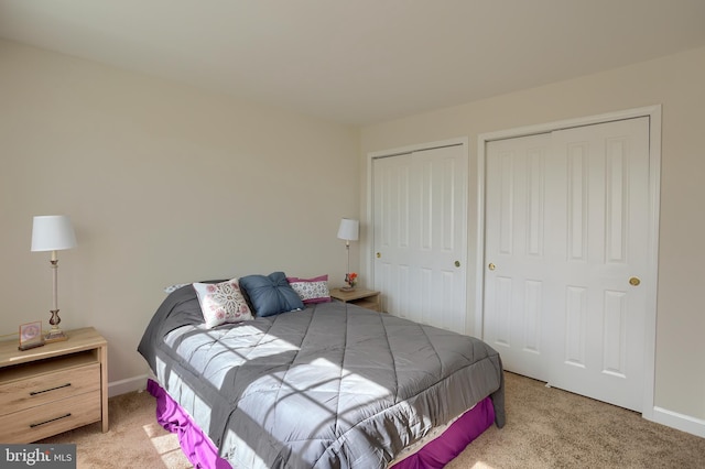 carpeted bedroom featuring baseboards and multiple closets