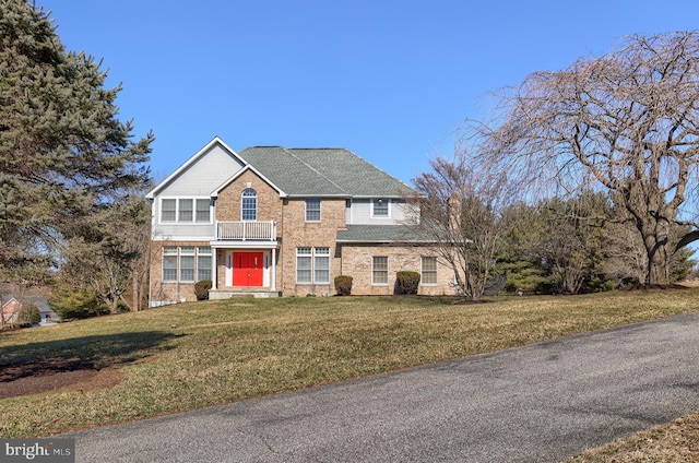 view of front of house featuring a shingled roof, a front yard, and a balcony