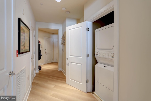 washroom featuring laundry area, baseboards, visible vents, stacked washer / drying machine, and light wood-type flooring