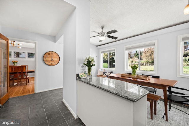 bar featuring a textured ceiling, lofted ceiling, ceiling fan with notable chandelier, dark tile patterned flooring, and baseboards