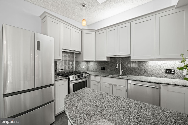 kitchen featuring a textured ceiling, stainless steel appliances, a sink, tasteful backsplash, and dark stone countertops