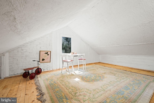 additional living space with vaulted ceiling, a textured ceiling, hardwood / wood-style flooring, and wooden walls