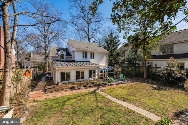 rear view of house featuring metal roof, a fenced backyard, a sunroom, a lawn, and a standing seam roof