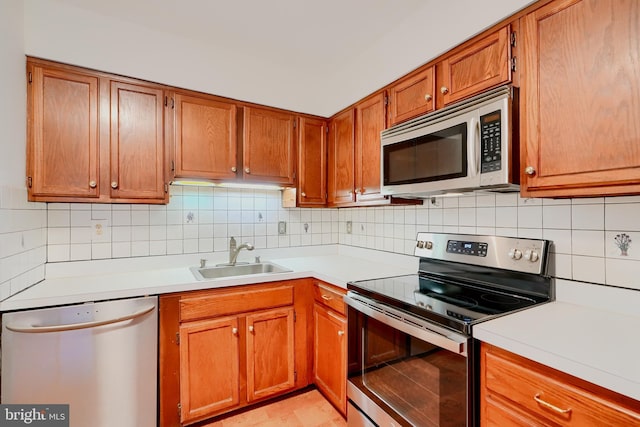 kitchen featuring light countertops, appliances with stainless steel finishes, a sink, and brown cabinets